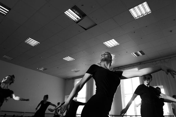 Group of people practicing synchronized movement exercises in a dark room with neon cyan outlines.
